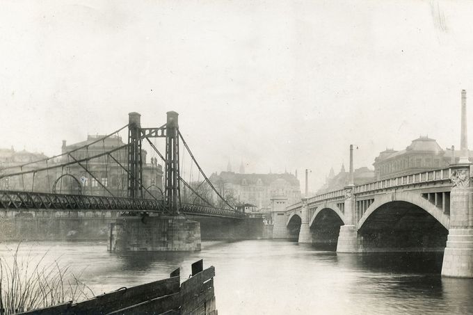Fotografie zachycující koexistenci Mánesova mostu a Rudolfovy lávky před jejím zbořením v roce 1914.