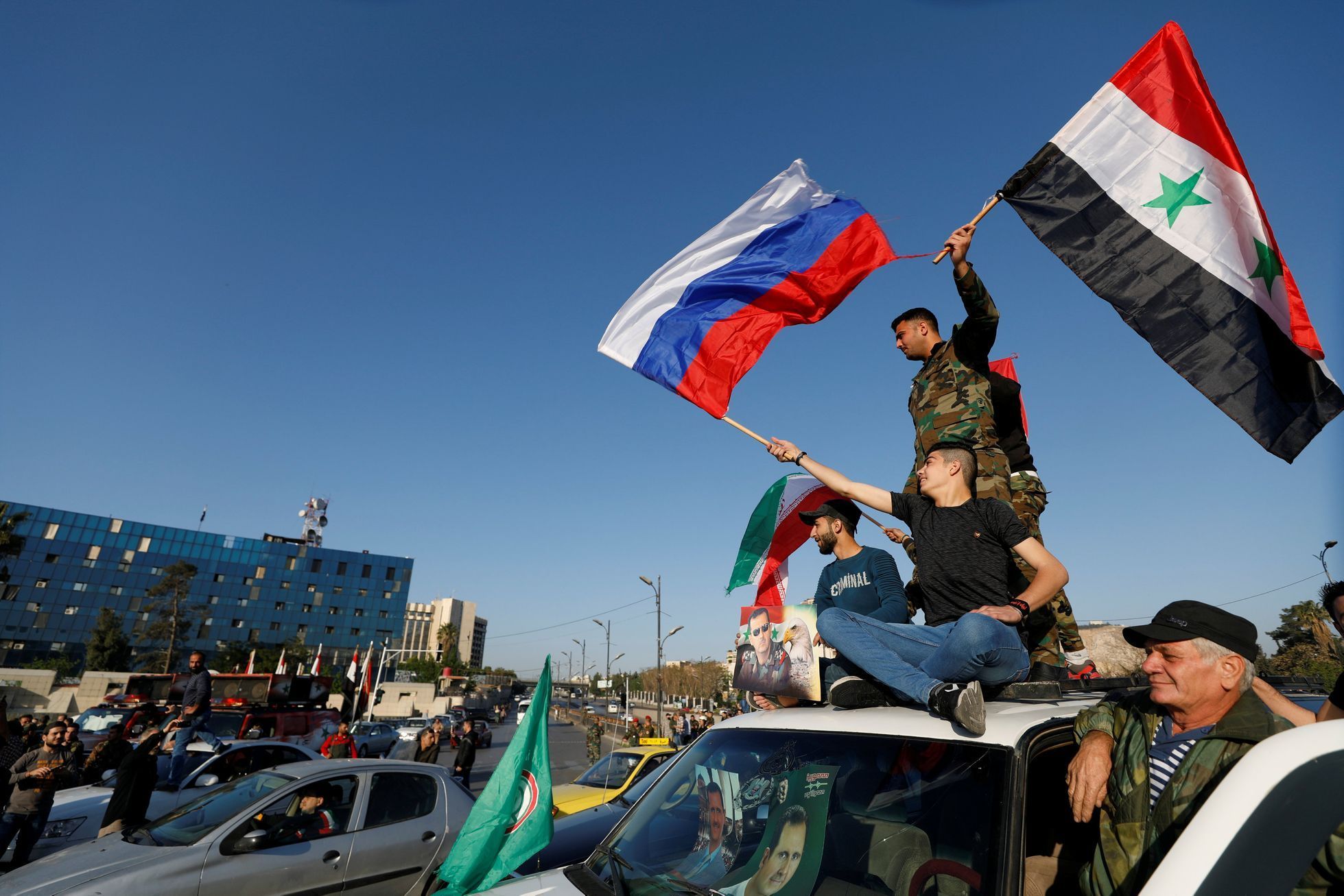 Lidé se syrskými, ruskými a íránskými vlajkami protestují proti náletům v Damašku.
