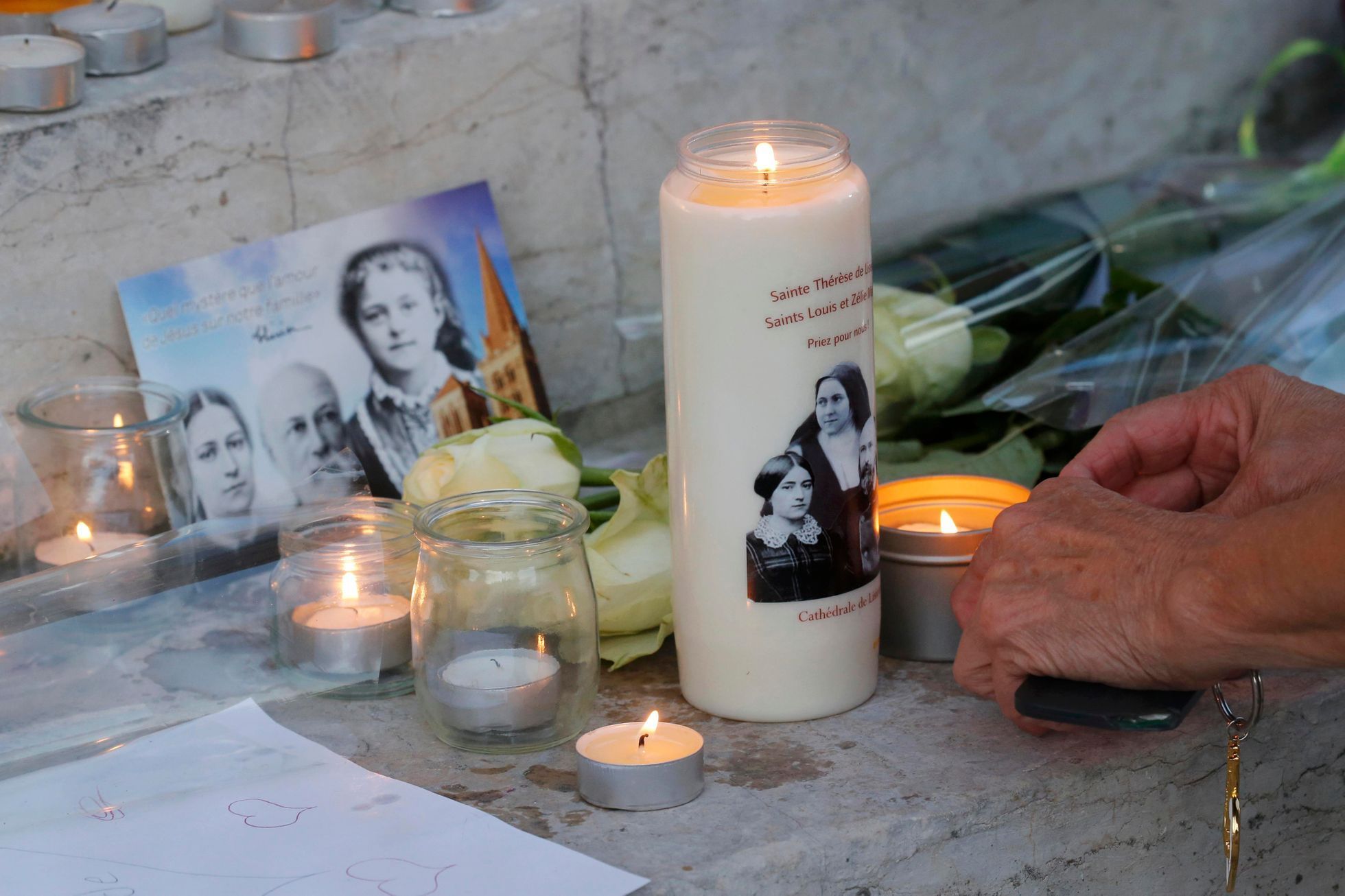 Žena zapaluje svíčku u radnice Saint-Etienne-du-Rouvray po teroristickém útoku v kostele