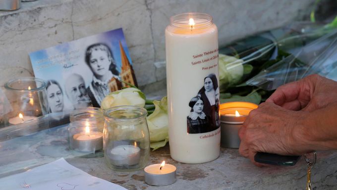 Žena zapaluje svíčku u radnice Saint-Etienne-du-Rouvray po teroristickém útoku v kostele.