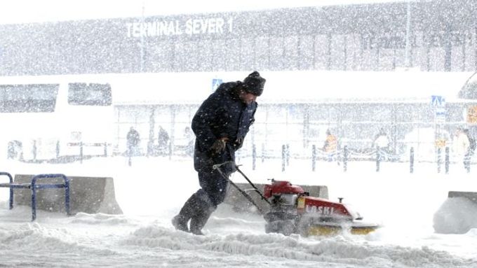 Pracovníci úklidových čet odklízejí sníh před terminálem pražského mezinárodního letište v Ruzyni, které bylo 12. března kvůli silnému sněžení mimo provoz.