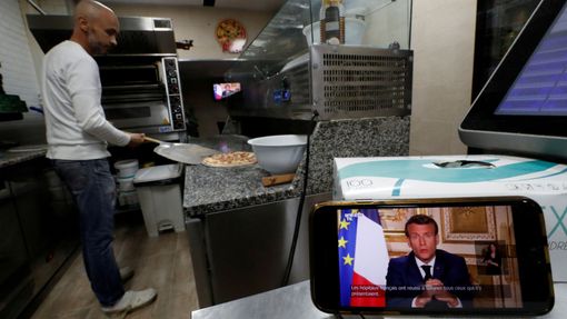 Výrobce pizzy ve francouzském Nice poslouchá Macronův projev.