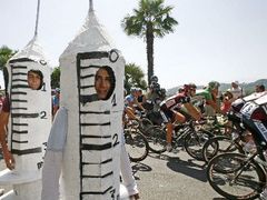 Peloton Tour de France projíždí kolem diváků převlečených za injekční stříkačky.
