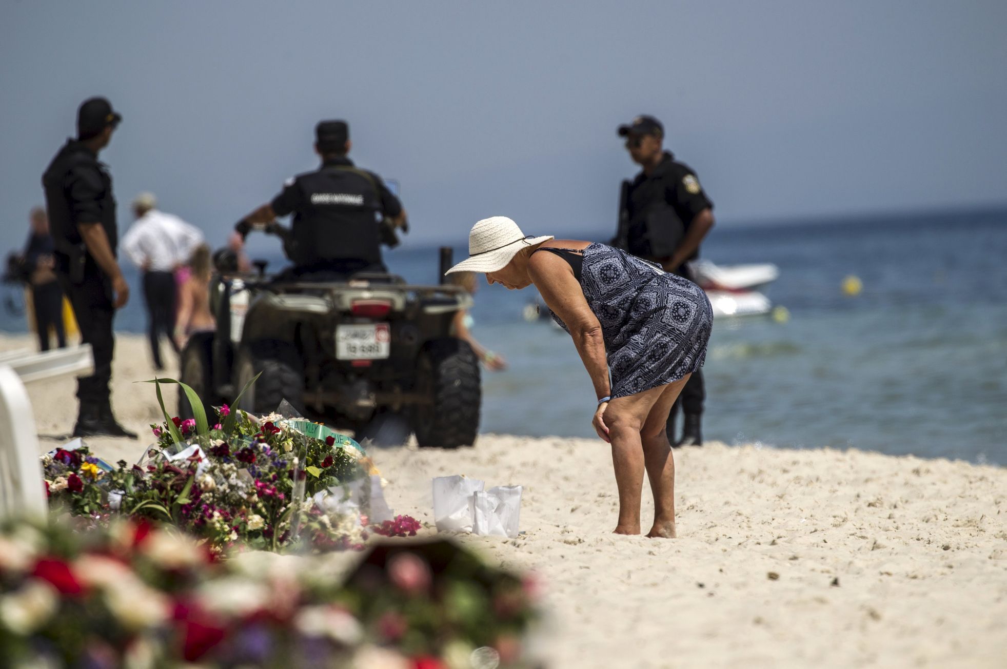 Turistka si prohlíží kondolence v blízkosti policejní hlídky.