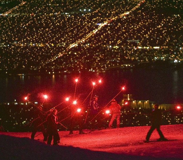 Lyžaři s pochodněmi sjíždí z kopce nad osvětleným Vancouverem, aby oslavili rok zbývající do zahájení olympijských her. | Foto: Reuters