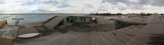 PLOT/ Maritime Youth Centre, Kopenhagen - celkový pohled  Malý jachtařský klub na předměstí Kodaně, který tvoří zborcené organické plochy, vytvářející jakousi dřevěnou krajinu pozvolna přecházející v mořský záliv. Konstrukce slouží zároveň jako úložiště kajaků a horní plocha jako vyhlídka či skluzavka pro děti. | Foto: Archív Galerie Jaroslava Fragnera