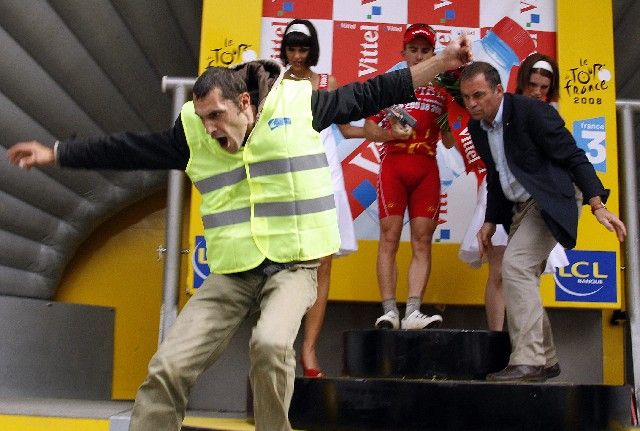 Třetí etapu Tour narušili demonstranti, tento se dostal na pódium při vyhlašování vítězů. Zasahovat se chystal i manažer PR slavného závodu Bernard Hinault (vpravo). | Foto: Reuters