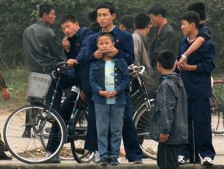 Severokorejci s odznaky strany ve městě Sinujiu na severokorejské straně řeky Ja-lu, která odděluje Severní Koreu od Číny | Foto: REUTERS / Reinhard Krause