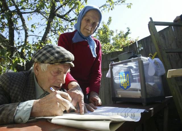 Žena pomáhá ve vesnici Lyčanka svému muži vyplnit volební lístky. | Foto: Reuters