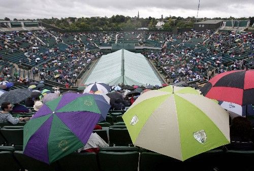 Diváci na centrálním kurtu Wimbledonu se musí schovávat pod deštníky, i v sobotu narušil program déšť. | Foto: Reuters