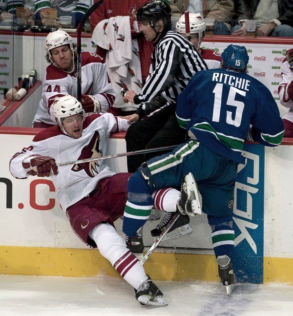 Já chci pryč! Rozhodčí se snaží utéct na hrazení před kolizí Byrona Ritchieho z Vancouveru Canucks (vpravo) a Keitha Ballarda z Phoenixu Coyotes. | Foto: Reuters