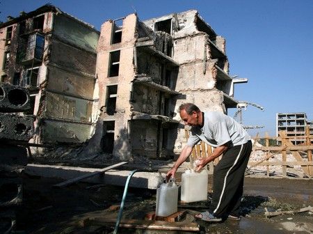 Muž plní kanystr před zničeným panelovým domem v Grozném. | Foto: REUTERS/Eduard Kornijenko