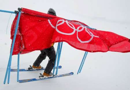 Pořadatel uklízí olympijský poutač z trati kombinačního sjezdu žen, který byl kvůli silnému větru zrušen. | Foto: Reuters