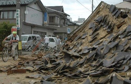 Muž na kole projíždí kolem zříceného domu ve městě Kašivazaki. Severozápad Japonska zasáhlo silné zemětřesení. | Foto: Reuters