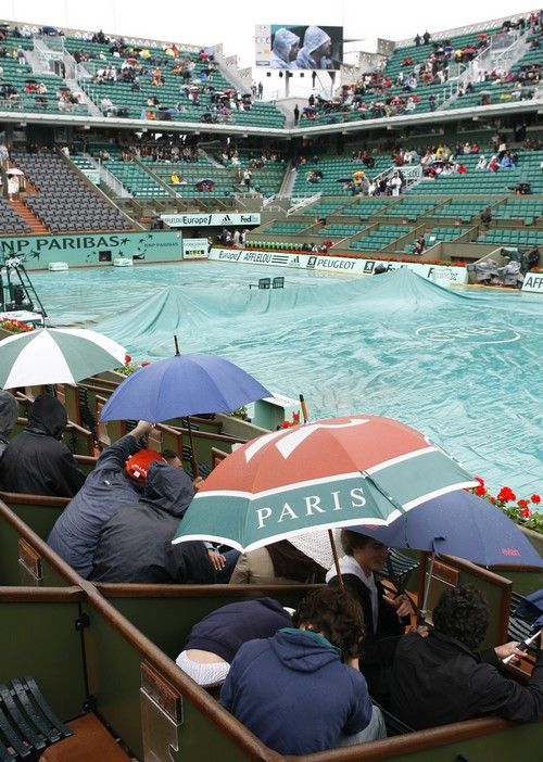 Diváci se schovávají pod deštníky v průběhu nedělního programu grandslamového French Open. | Foto: Reuters