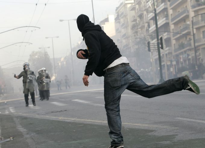 Účastník nedělní demonstrace v Athénách hází kámen na policisty. Ti museli použít vodní děla a slzný plyn | Foto: Reuters