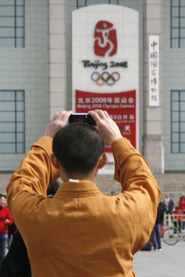 To jsou paradoxy. Budhistický mnich si fotí tabuli odpočítávající čas do začátku olympiády. | Foto: Reuters