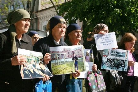 Ženy před soudní síní ve Vladikavkazu drží fotografie obětí beslanského útoku. Žena drží nápis: "Kulajeve a tobě podobní, budete prokletí na věky" | Foto: Reuters