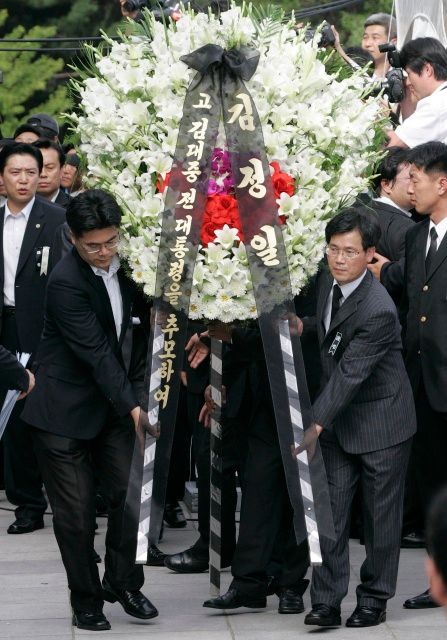 Vyslanci Kim Čong-ila v černých oblecích položili u budovy Národního shromáždění věnec. Nese jméno severokorejského vůdce. | Foto: Reuters