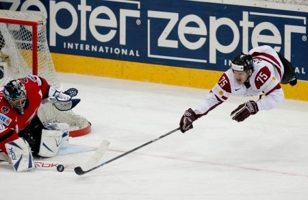 Lotyšský hokejista Aleksandrs Jerofejevs v akrobatické pozici ohrožuje rakouského gólmana Bernda Bruckler. | Foto: Václav Rojík