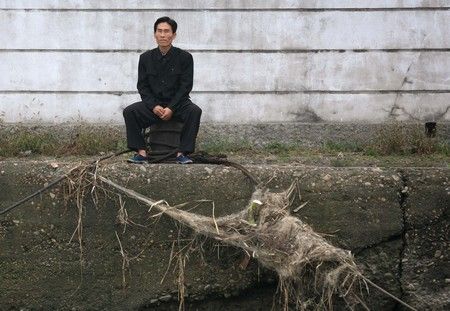 Muž sedí ve městě Sinujiu na severokorejské straně řeky Ja-lu, která odděluje Severní Koreu od Číny | Foto: REUTERS / Reinhard Krause