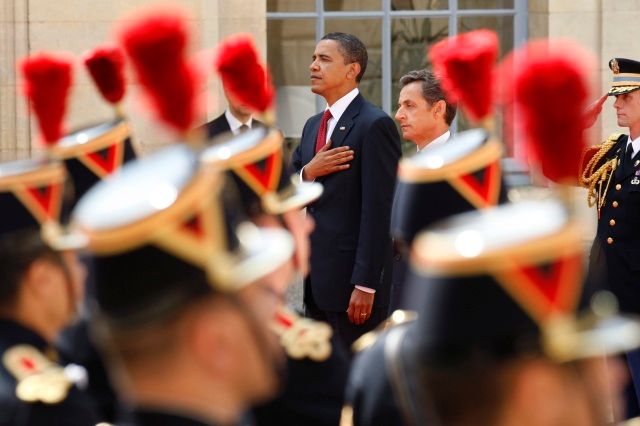 Barack Obama a Nicolas Sarkozy naslouchají státním hymnám během předchozí ceremonie v Caen. Později se Obama přesune na oslavu výročí. | Foto: Reuters