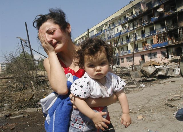 Žena s dítětem prchají z poničeného domu. | Foto: Reuters