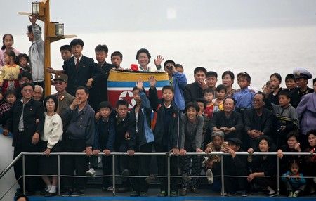 Lidé drží severokorejskou vlajku během plavby na řece Ja-lu, která odděluje Severní Koreu od Číny | Foto: REUTERS / Reinhard Krause