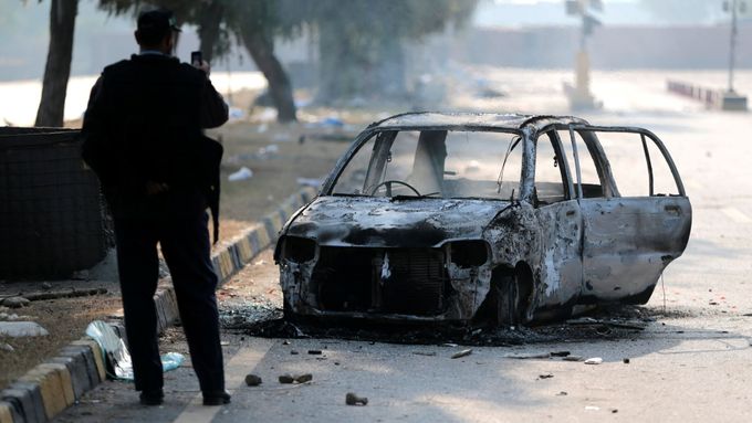 Policista fotografuje spálené auto po střetech u křižovatky Faizabád v Islámábádu.