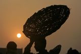 Silueta prodejce, který nese při východu slunce v pákistánském Láhauru nad hlavou koš.