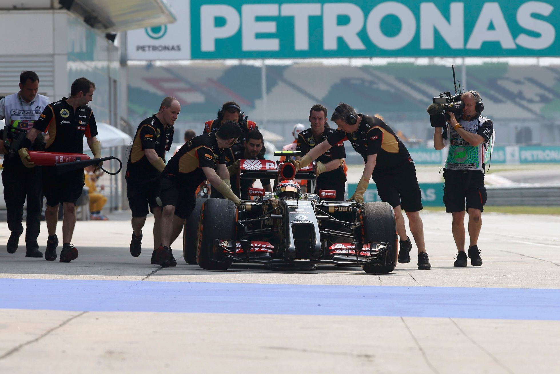 Mechanics push the car of Lotus Formula One driver Maldonado of Venezuela down the pit lane during the first practice session of the Malaysian F1 Grand Prix at Sepang International Circuit outside Kua