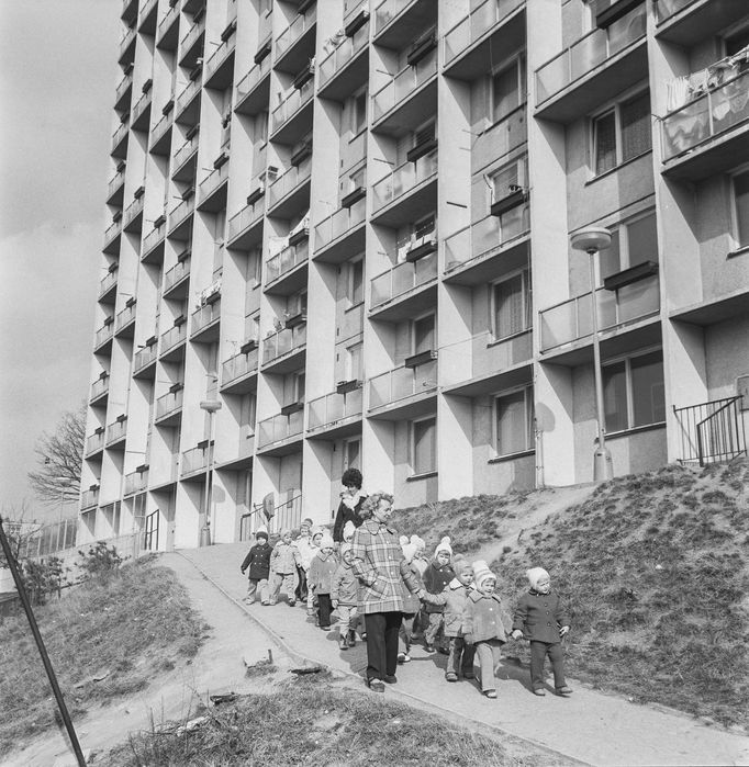 Děti z mateřské školky v doprovodu učitelek kráčí okolo tehdy nově postavených panelových domů v Adamově, rok 1975.