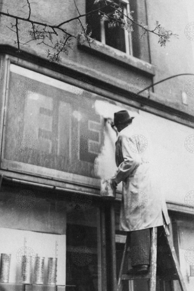 Odstraňování německých nápisů nad obchodem na Vinohradech ve večerních hodinách dne 4. 5. 1945