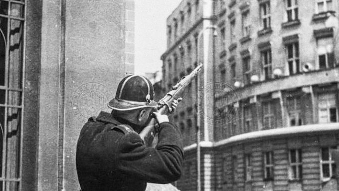 Četník se snaží na rohu Blanické a Slezské ulice v Praze zlikvidovat německého odstřelovače. Dne 5. května 1945.
