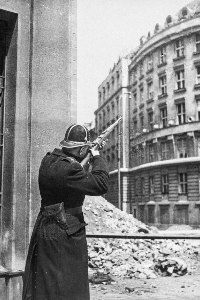 Četník se snaží na rohu Blanické a Slezské ulice v Praze zlikvidovat německého odstřelovače. Dne 5. května 1945.