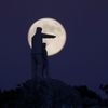 Statue of a man and a boy, is silhouetted against the supermoon as it rises at the Sierra de las Nieves nature park and biosphere reserve between El Burgo and Ronda