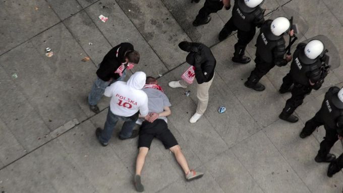 Po násilnostech mezi polskými a ruskými fanoušky: na zemi leží zraněný polský fanda, kordon policistů ve střehu.