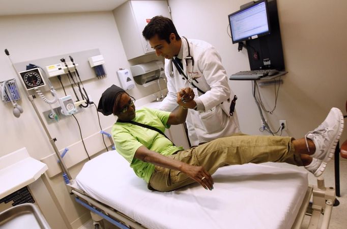 Patient Sharon Dawson Coates is helped to sit up after having her knee examined by Dr. Nikhil Narang at University of Chicago Medicine Urgent Care Clinic in Chicago June 28, 2012. A sharply divided U.S. Supreme Court on Thursday upheld the centerpiece of President Barack Obama's signature healthcare overhaul law that requires that most Americans get insurance by 2014 or pay a financial penalty. REUTERS/Jim Young (UNITED STATES - Tags: POLITICS HEALTH) Published: Čer. 28, 2012, 7:41 odp.