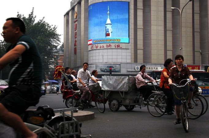 Commuters ride bicycles and electric bikes as they pass a large screen displaying pictures of China's recent spacecraft launch in the centre of Beijing June 18, 2012. A Chinese spacecraft carried out a manned docking with an experimental space module on Monday, the latest milestone in China's ambitious effort to build a space station. REUTERS/David Gray (CHINA - Tags: SOCIETY SCIENCE TECHNOLOGY) Published: Čer. 18, 2012, 10:17 dop.