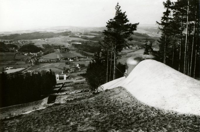 Pohled od čtyřstřílnového pěchotního zvonu objektu N-S 81 ,,Jirásek" (odlitého Báňskou a hutní společností v Třinci pod číslem 66 v rámci druhé výrobní série) na sousední izolovaný pěchotní srub N-S 82 ,,Březinka" a dále pokračující linii pěchotních srubů přehrazujících údolí Metuje u Bělovsi a stoupající směrem k Babí.