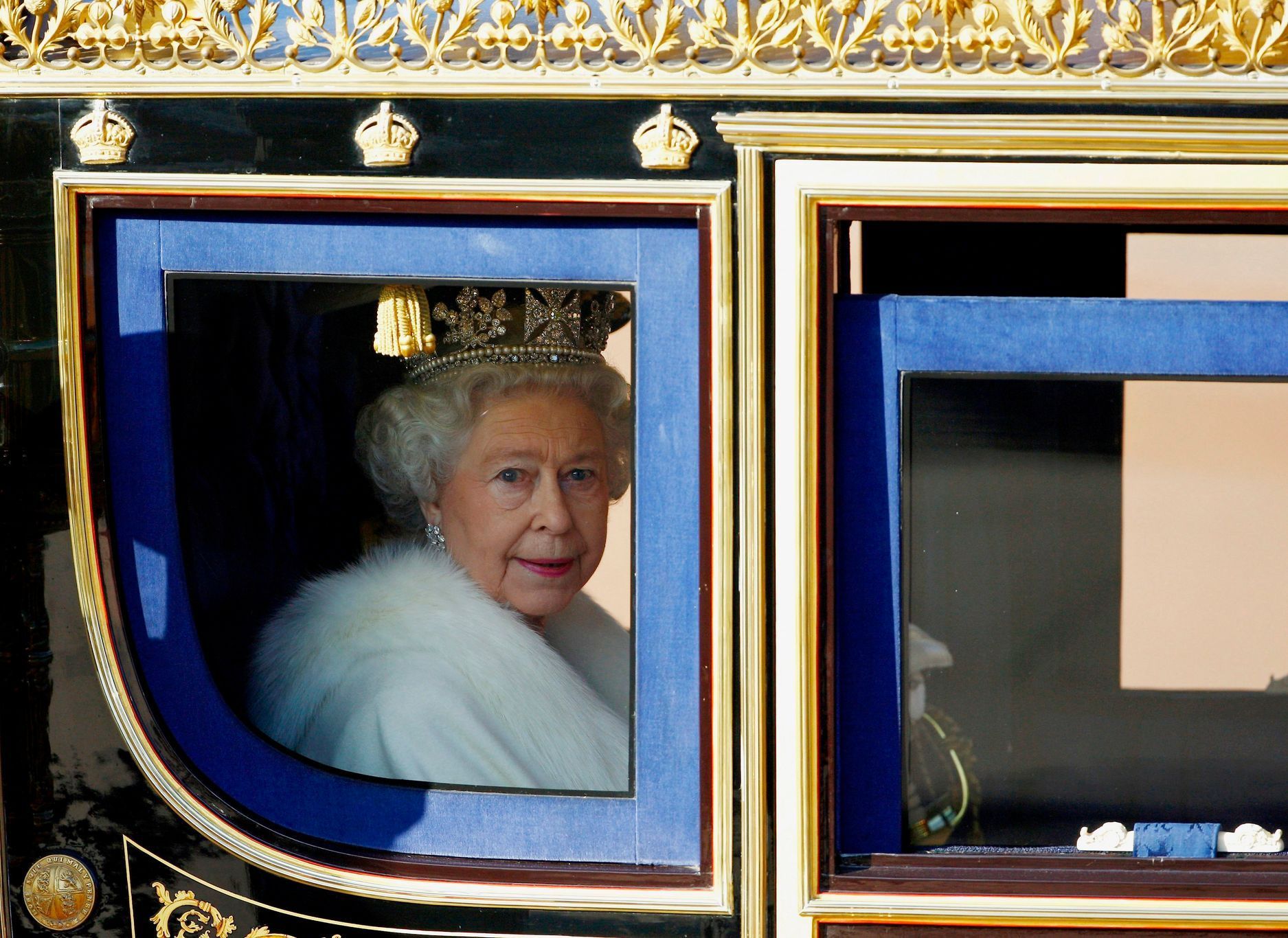Královna Alžběta II. vyhlíží ze svého kočáru