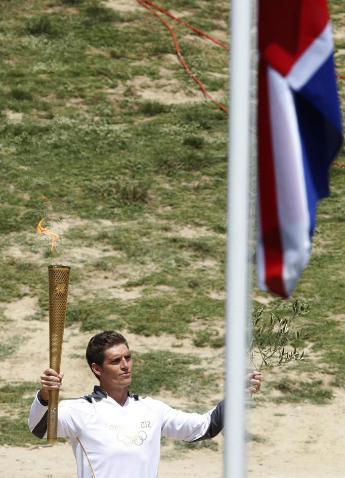 Spyridon Gianniotis, Greece's world champion of swimming, stands next to a Union flag as he holds up the Olympic flame and an olive branch during the torch lighting ceremony of the London 2012 Olympic Games at the site of ancient Olympia in Greece May 10, 2012. REUTERS/Mal Langsdon (GREECE - Tags: SPORT OLYMPICS) Published: Kvě. 10, 2012, 10:45 dop.