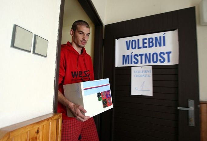 Člen volební komise Jakub Piškora přináší do volební místnosti v obci Tuchlovice zapečetěnou volební urnu.