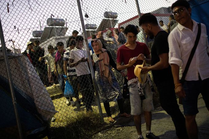 Migranti opouští uprchlický tábor dírou v plotě.
