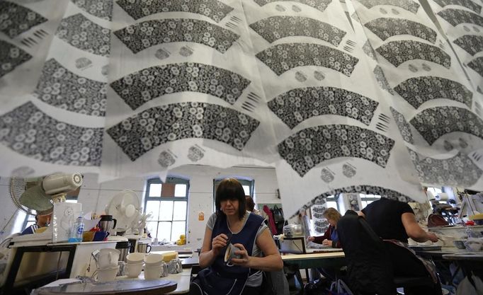 A worker applies tissue paper transfers to a cup, as others hang to dry in a workshop at the Middleport pottery in Stoke-on-Trent, central England January 22, 2013. The pottery which dates back to 1888 and was rescued from closure in 2009, continues to use traditional methods to produce its range of ceramics and famous Burleigh Ware pottery. REUTERS/Phil Noble (BRITAIN - Tags: BUSINESS EMPLOYMENT SOCIETY) Published: Led. 22, 2013, 4:33 odp.