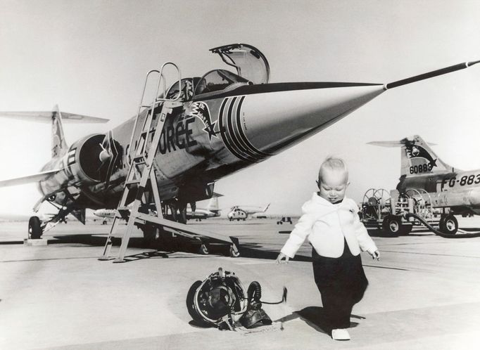 Dítě stojící u helmy a kyslíkové masky z letounu USAF Lockheed F-104C Starfighter, který je na snímku vidět v pozadí, USA, rok 1960.