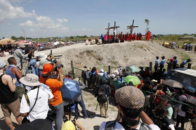 People watch as Ruben Enaje (C), 52, who is portraying Jesus Christ for the 27th time, hangs on a cross beside two men, who are portraying Dismas and Gestas, during a Good Friday crucifixion re-enactment in San Pedro Cutud town, Pampanga province, north of Manila March 29, 2013. The Roman Catholic church frowns on the gory spectacle held in the Philippine village of Cutud every Good Friday but does nothing to deter the faithful from emulating the suffering of Christ and taking a painful route to penitence. Holy Week is celebrated in many Christian traditions during the week before Easter. REUTERS/Romeo Ranoco (PHILIPPINES - Tags: RELIGION SOCIETY) Published: Bře. 29, 2013, 8:06 dop.