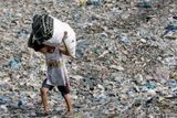 Chlapec nese pytel dřevěného uhlí přes skládku odpadu v Manile.