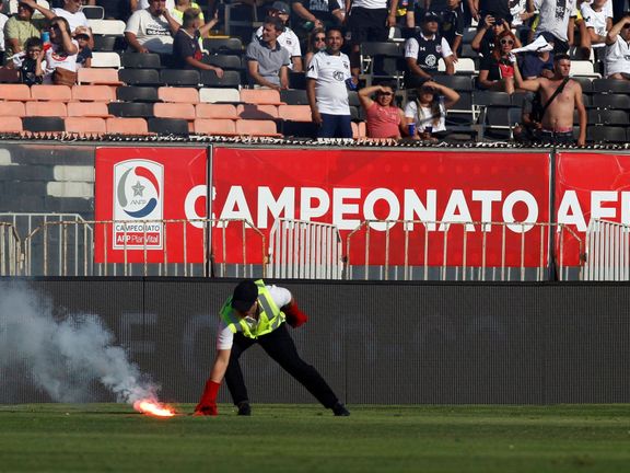 Jeden z pořadatelů likviduje světlici, kterou hodili na trávník fanoušci při utkání chilské fotbalové ligy mezi týmy Colo Colo a Universidad de Católica