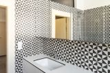 Geometrický obklad vymezuje nejenom kuchyňský kout v obývacím prostoru, stejný vzor se opakuje i v koupelně, doplněn bílým nábytkem, který vizuálně zvětšuje prostor.